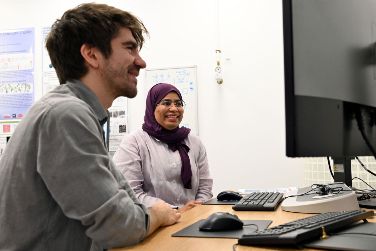 Two students sit at a computer and are smiling
